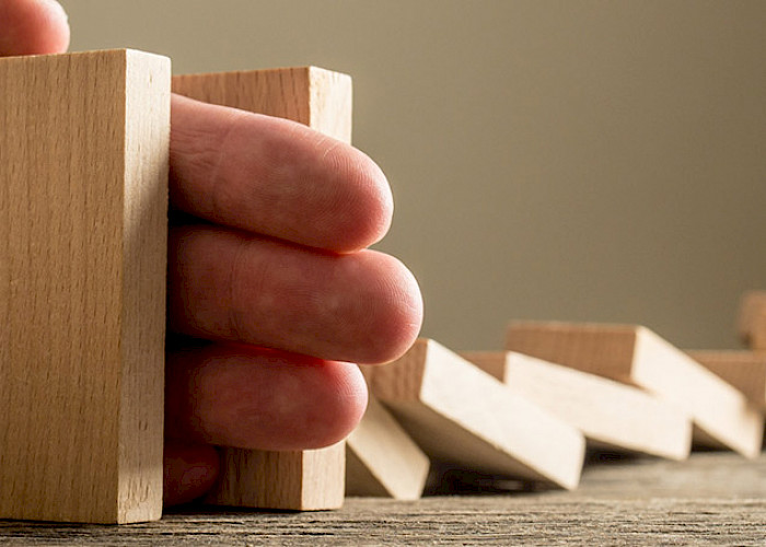 Krisen / Krisenintervention Hand die umfallende Dominosteine aufhält - ©